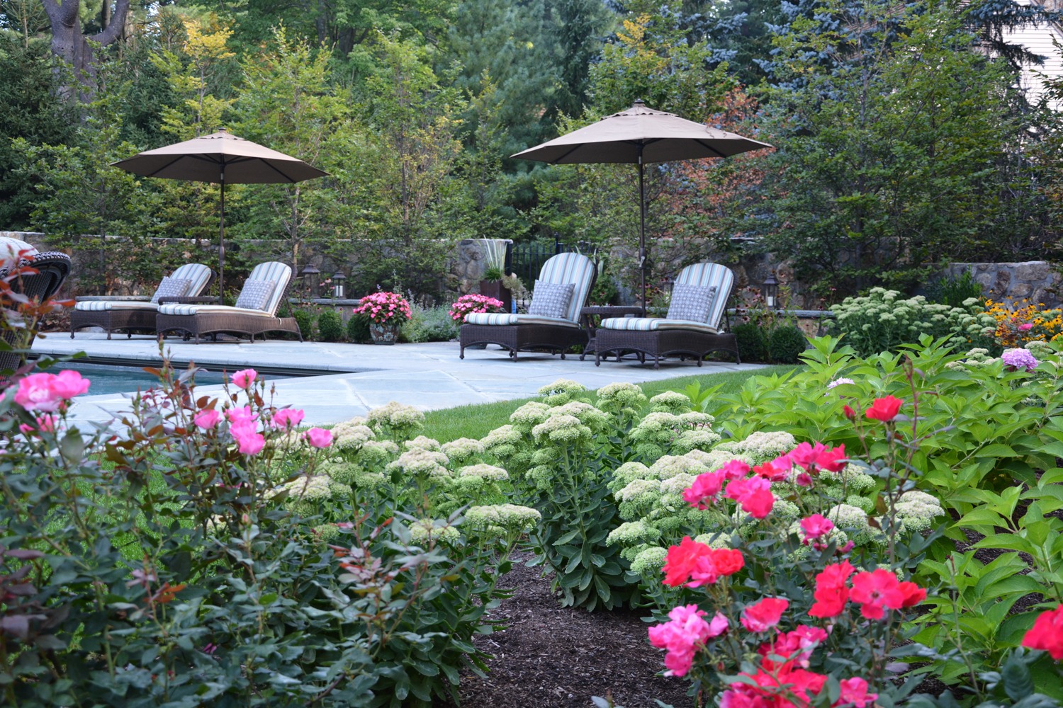 An inviting garden with colorful flowers, greenery, and a seating area with lounge chairs under umbrellas, suggesting a peaceful outdoor relaxation space.