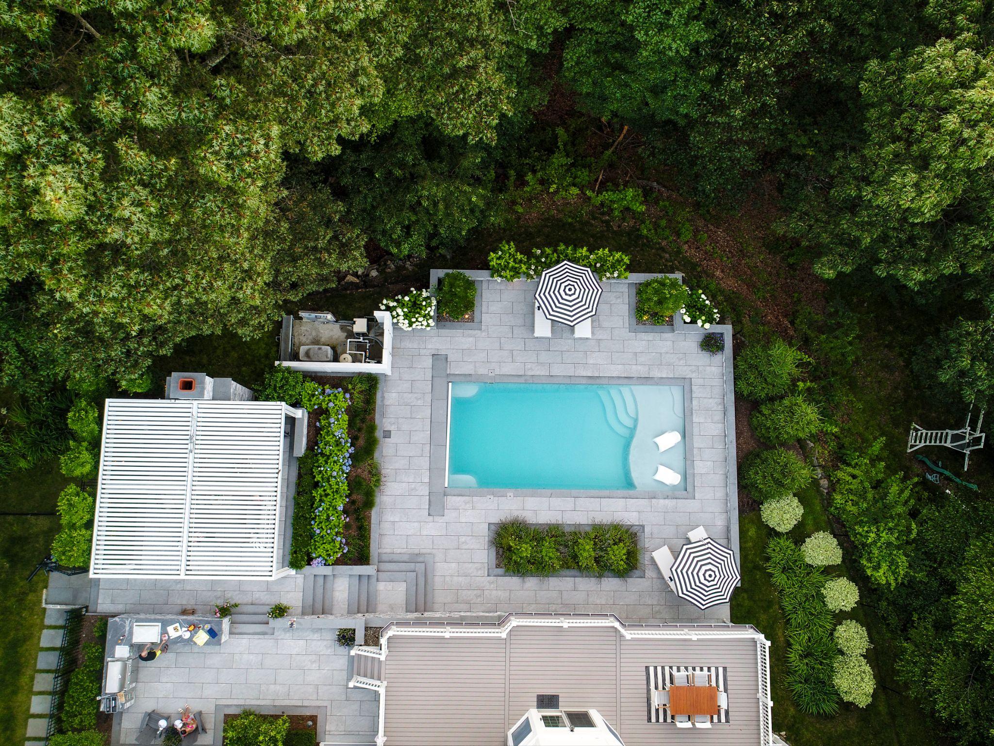 Aerial view of a modern residential pool terrace with integrated softscaping, patio spaces, and surrounding woodland