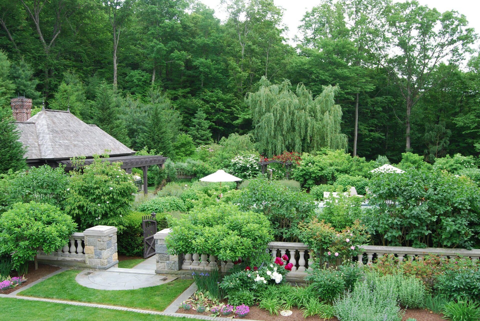 Formal garden with stone walls, layered greenery, and wooded backdrop