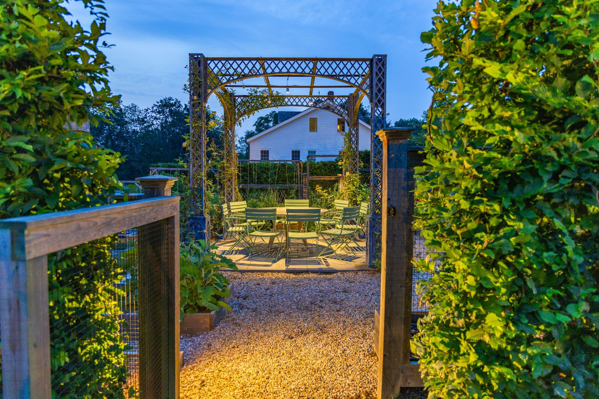 Garden arbor with climbing plants, gravel pathway, and outdoor dining area integrated into a residential landscape