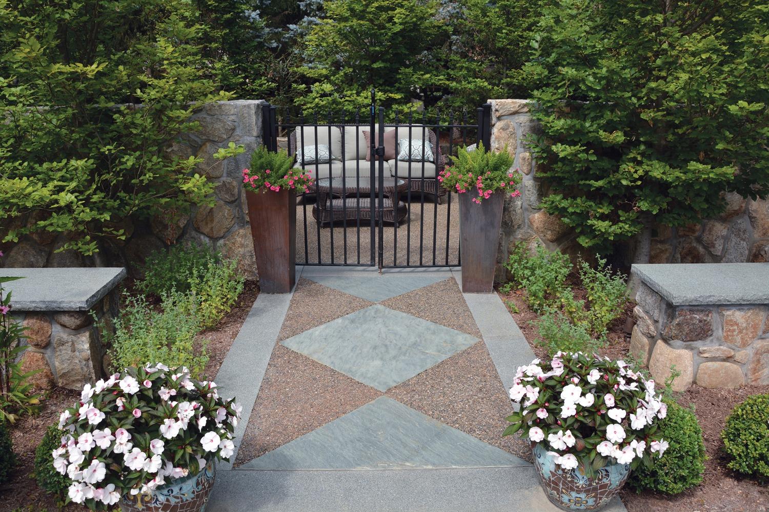 Garden gate leading to a private seating area with stone walls, container plantings, and softscaped borders