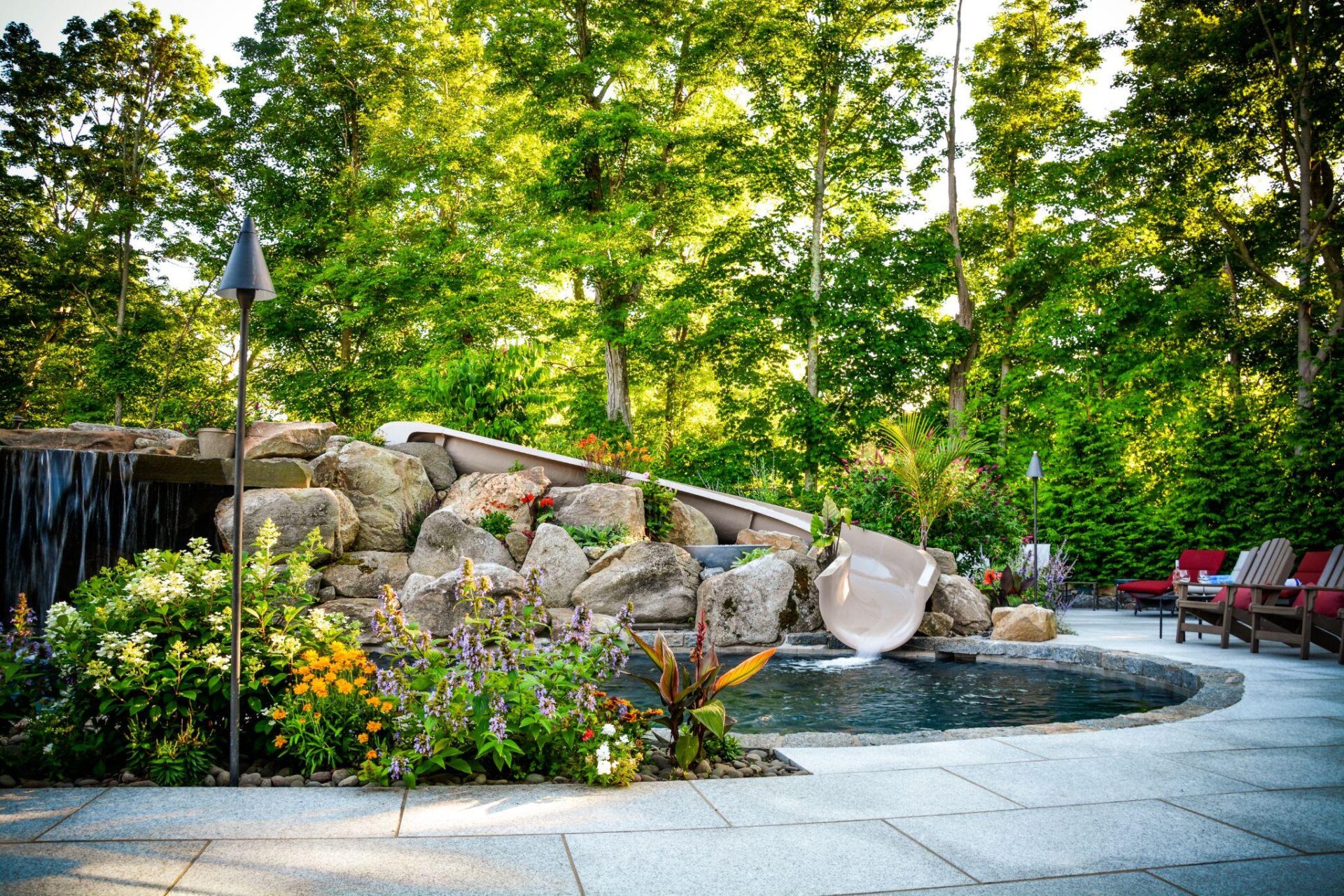 Luxury residential pool with natural stone waterfall, integrated slide, and layered softscaping surrounded by mature trees