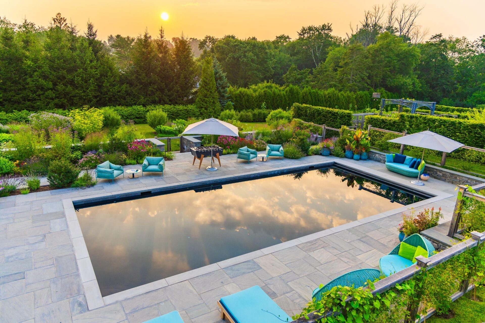 Modern pool landscape with stone patio and outdoor seating at sunset